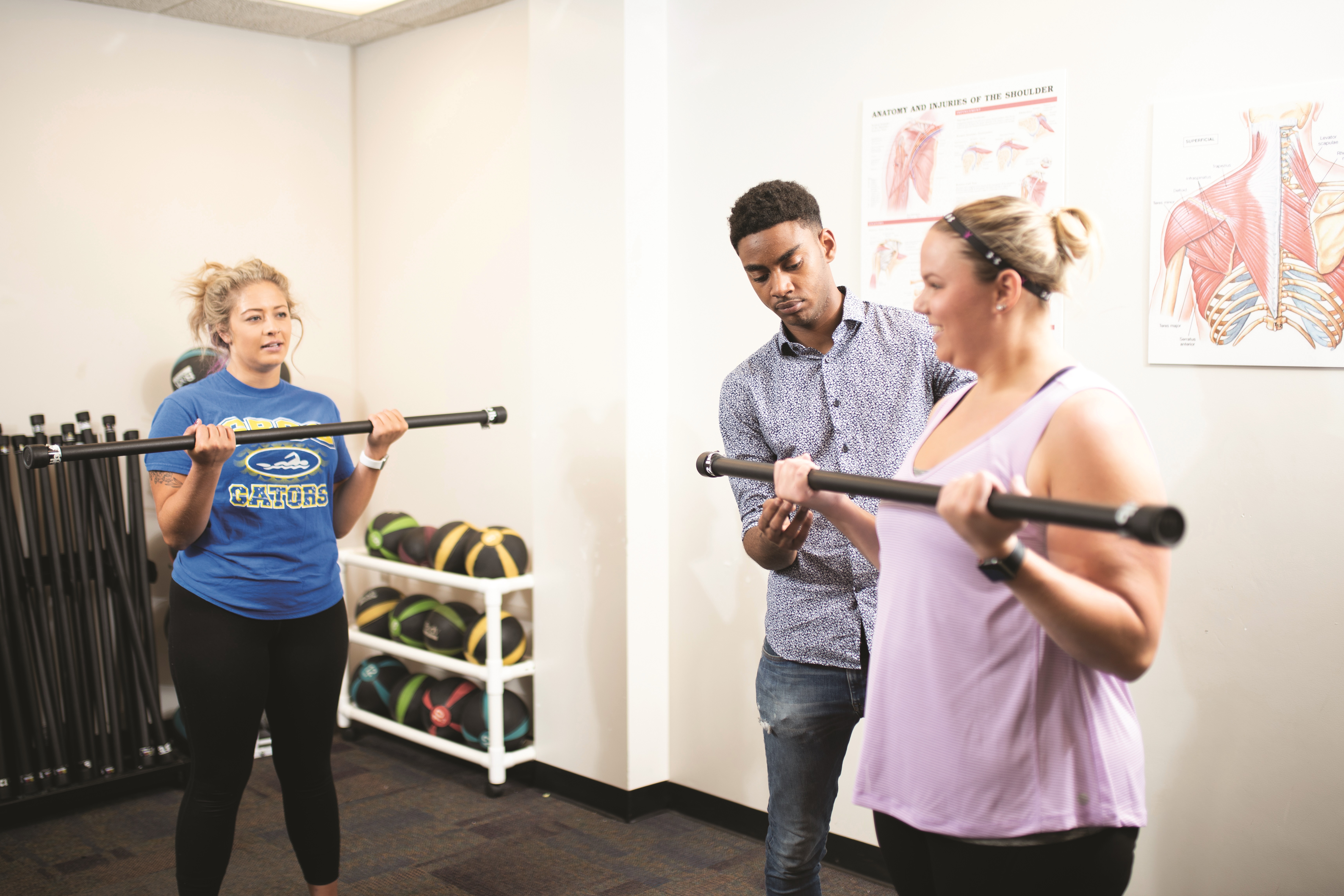 Three GRCC students exercising with weighted poles in a classroom