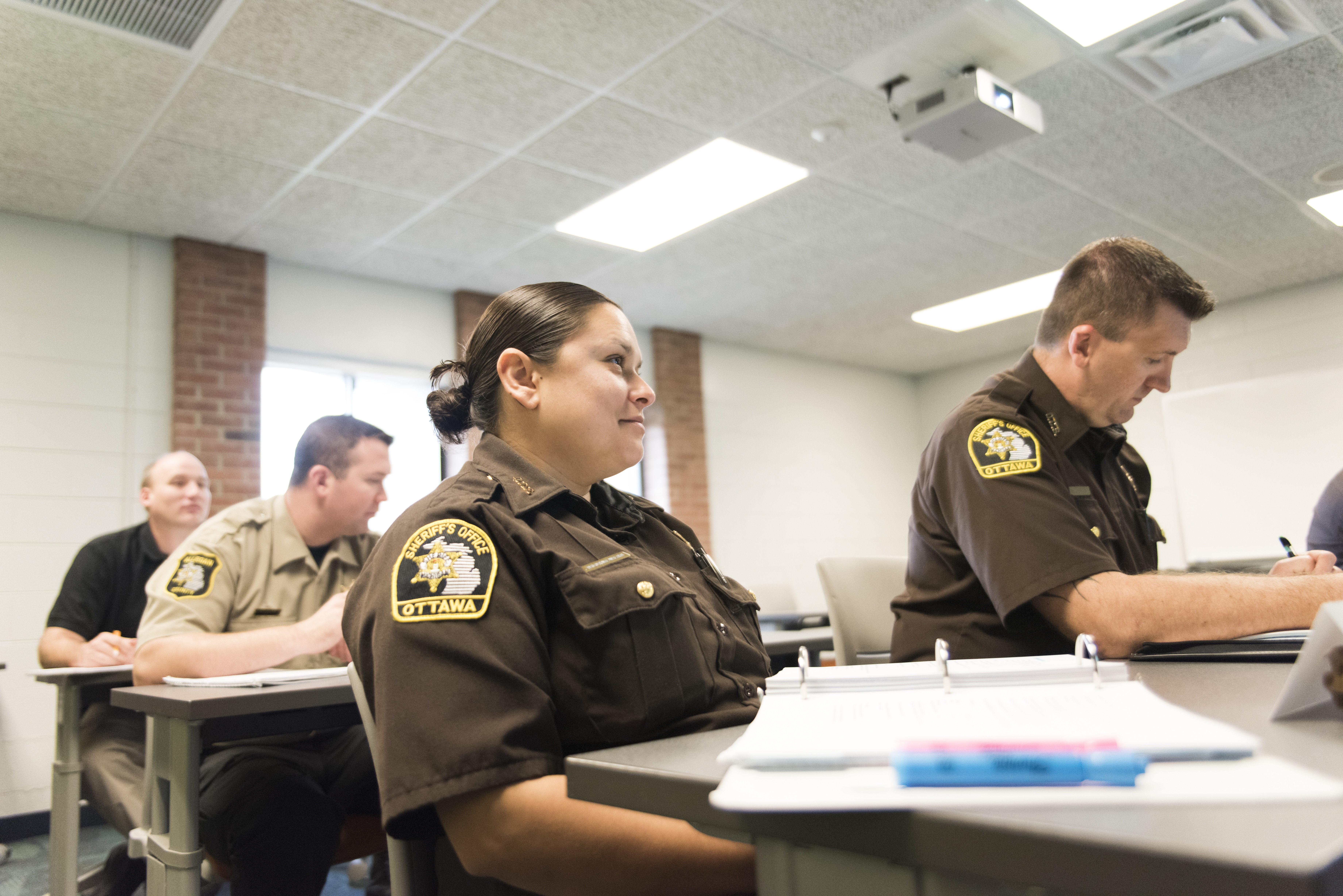 Law Enforcement Officers sitting in classroom.  One officer has a notebook open in front of her.