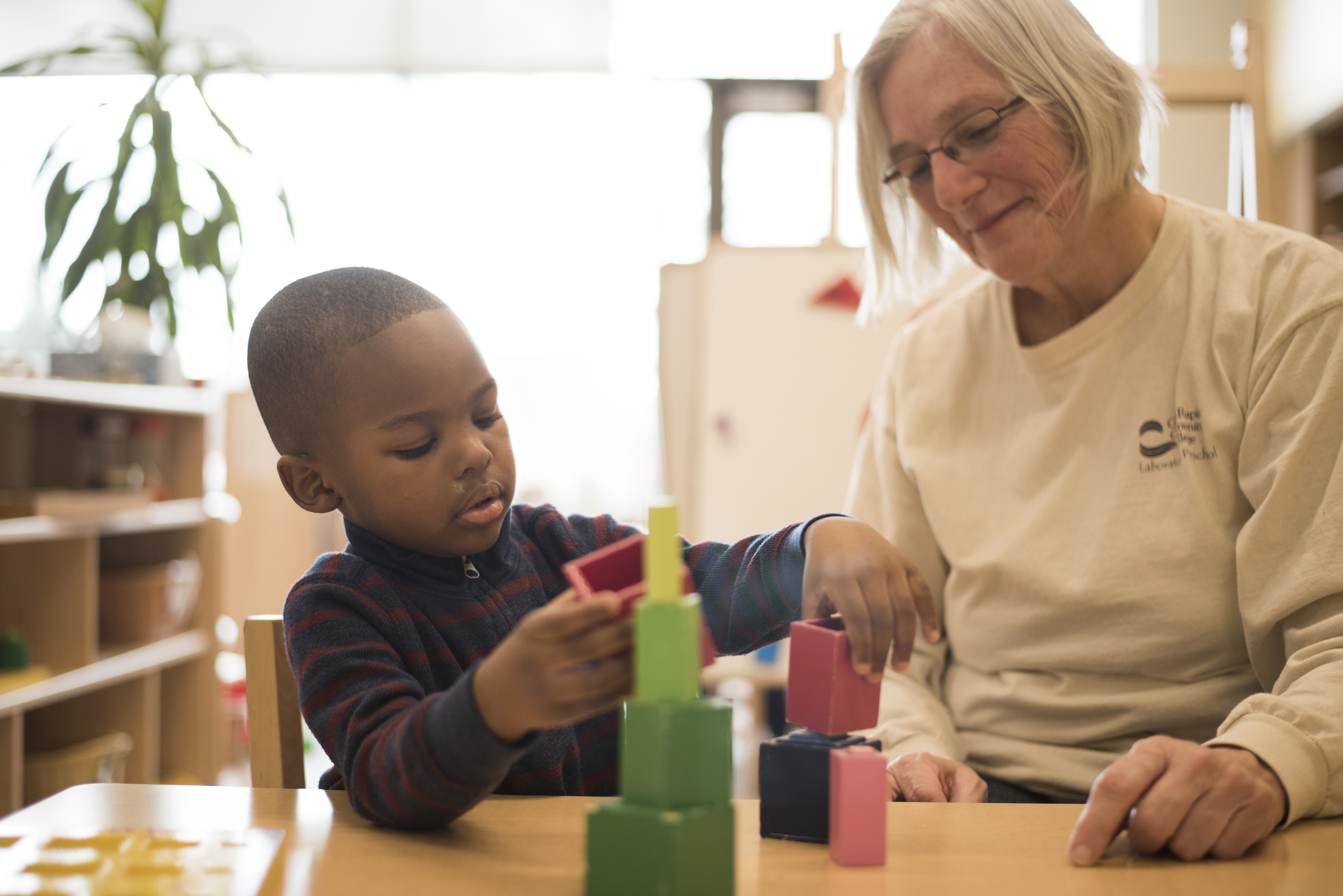A lady sitting at a table building a cup tower with a young child.